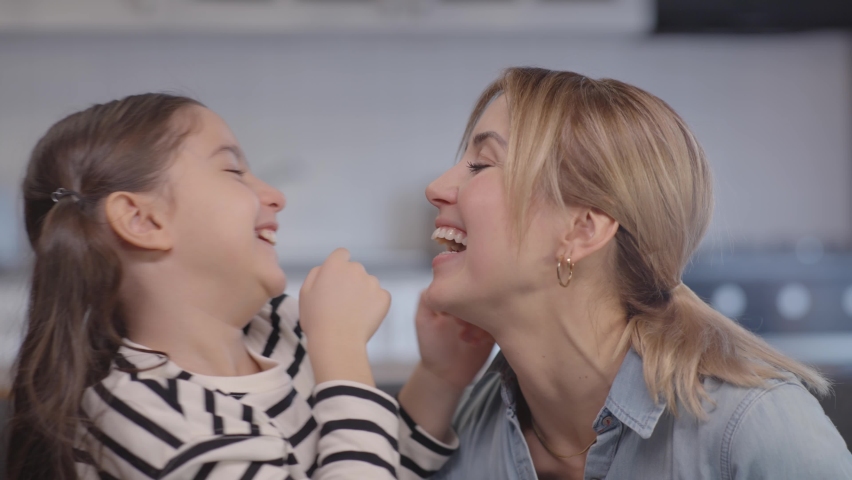 Happy little cute girl hugging, kissing and hugging her mother, having fun together, tying and laughing. Portrait of daughter and mother having nice time at home living room. Slow motion video. | Shutterstock HD Video #1068643487