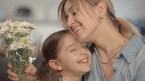 The 6-7 year old girl gives a bouquet of daisies and hugs her mother. Mom's birthday or Mother's Day. Slow motion video.