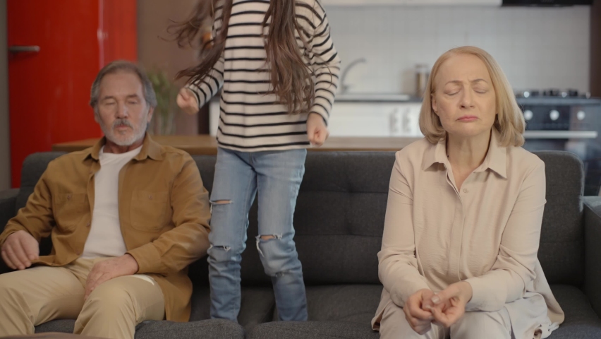 Desperate grandmother and grandpa sitting on the sofa are harassed by their naughty little daughter grandson at home. Royalty-Free Stock Footage #1068643523