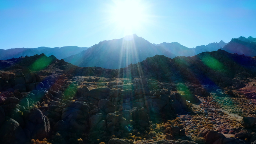 Aerial shot of rocks at famous natural landmark against sky, drone flying backward from rocky mountains on sunny day - Alabama Hills, California