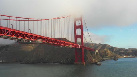 Aerial panning shot of Golden Gate Bridge over sea against sky, drone flying by famous landmark under fog over bay - San Francisco, California