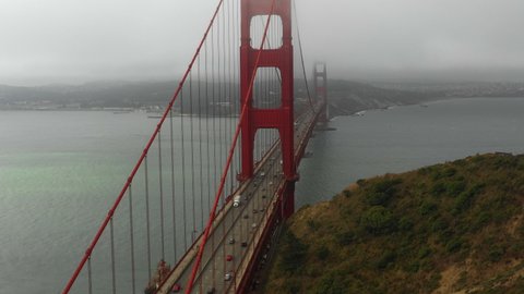 Aerial panning shot of Golden Gate Bridge over sea under foggy weather, drone flying over vehicles on famous bridge over bay - San Francisco, California