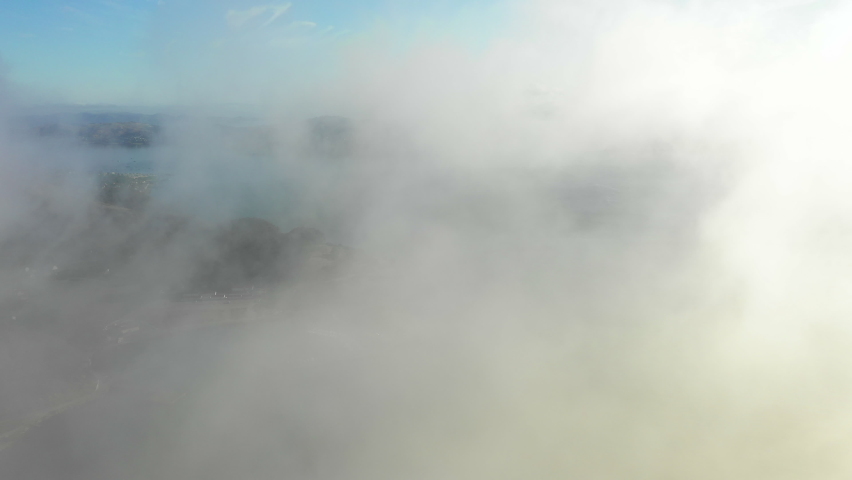 Aerial panning shot of landscape and bay under foggy weather against sky, drone flying over harbor near mountains - San Francisco, California