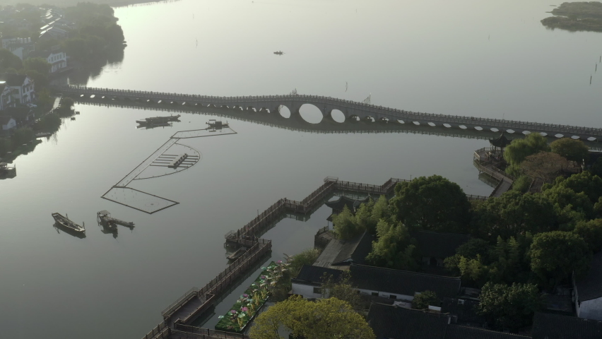 Aerial shot of footbridge over lake during sunset, drone flying forward over water - Suzhou, China
