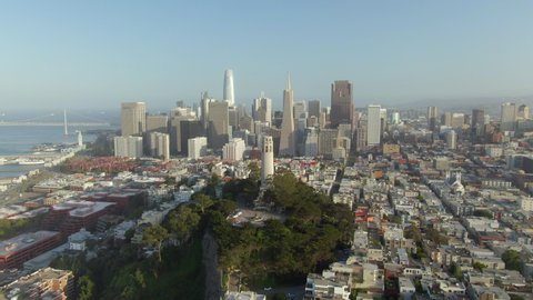 Aerial approach of the soaring downtown skyline with a tilt down to quaint, cozy, and historic Telegraph Hill and Coit Tower - San Francisco, California