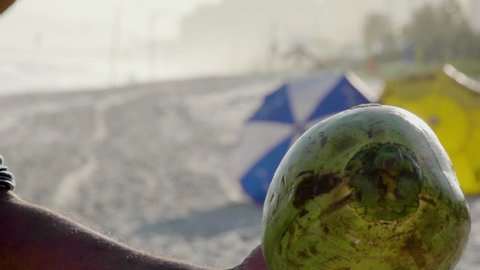 Close-up of opening coconut with machete at beach, slow motion.