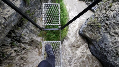 Pov: Person Steps Gingerly Across Narrow Rope Bridge Over Roaring River And Sharp Cliffs