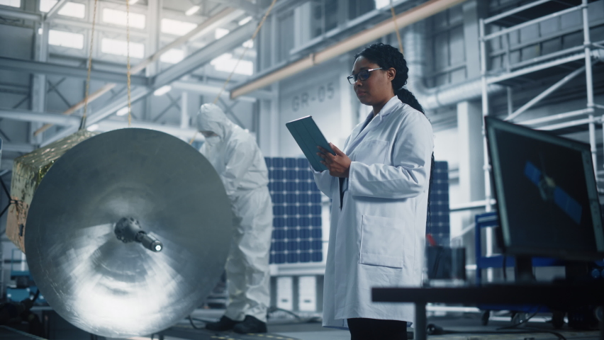 Female Engineer Uses Tablet Computer while Working on Satellite Construction. Aerospace Agency Manufacturing Facility: Scientists Build, Assemble Spacecraft for Space Exploration, Observation Mission