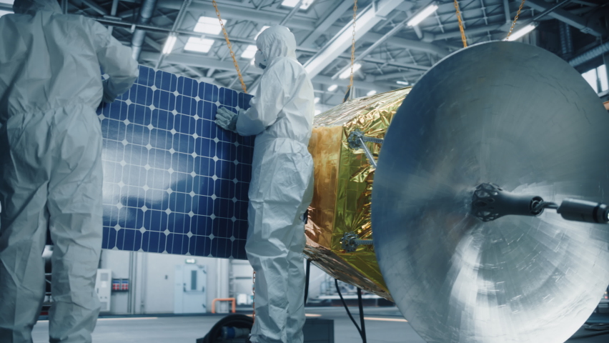Engineer and Technician in Protective Suits Working on Satellite Construction. Aerospace Agency: Team of Scientists Fixing Solar Panel Wings to Spacecraft. International Space Exploration Mission