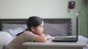 Asian child student or kid girl chin on arm to tired and watching computer notebook for e-learning communication or study online and people learn from home to education play laptop by back to school