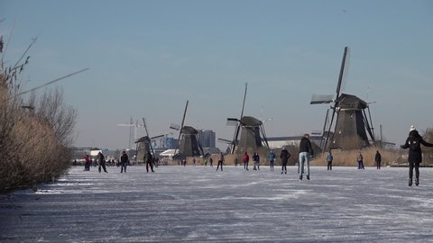 KINDERDIJK, NETHERLANDS – 13 FEBRUARY 2021: Beautiful Winter scene as people are ice skating on frozen canals in Kinderdijk town. Tradition, culture, and leisure activities in the Netherlands. 
