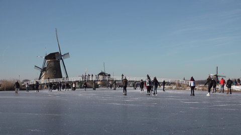 KINDERDIJK, NETHERLANDS – 13 FEBRUARY 2021: People ice skate on frozen canals with beautiful historic windmills as backdrop. A welcome break from continuiing lockdown measures in the Netherlands.
