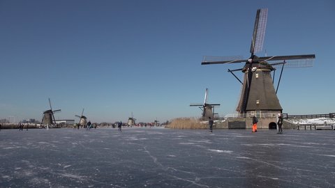KINDERDIJK, NETHERLANDS – 13 FEBRUARY 2021: People ice skate on frozen canals past windmills, enjoying a traditional Dutch sport (a welcome break from Covid-19 lockdown)