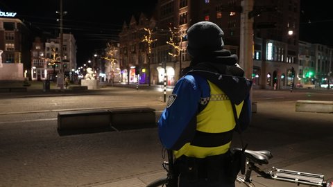 AMSTERDAM, NETHERLANDS – 5 MARCH 2021: Municipality enforcer with bicycle patrols streets in Amsterdam, during evening curfew in the Netherlands (Covid-19 coronavirus second wave in Europe).