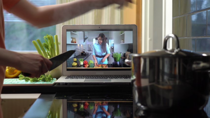 A young woman watching a online stream broadcast video blog tutorial about tasty and healthy food using laptop and cooking a meal at the home kitchen | Shutterstock HD Video #1068668921