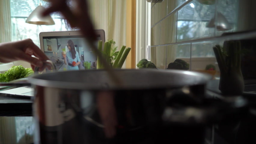 A young woman watching a online stream broadcast video blog tutorial about tasty and healthy food using laptop and cooking a meal at the home kitchen Royalty-Free Stock Footage #1068668984