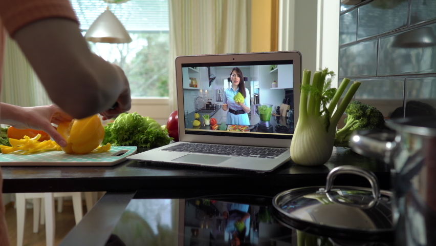 A young woman watching a online stream broadcast video blog tutorial about tasty and healthy food using laptop and cooking a meal at the home kitchen Royalty-Free Stock Footage #1068668984