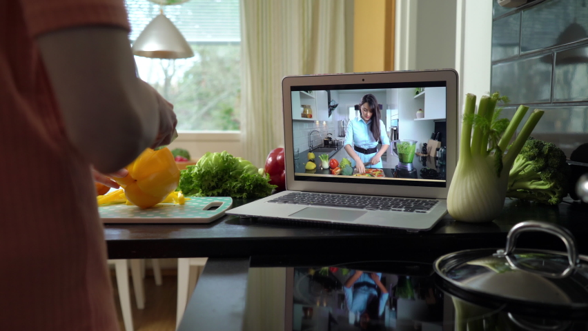 A young woman watching a online stream broadcast video blog tutorial about tasty and healthy food using laptop and cooking a meal at the home kitchen | Shutterstock HD Video #1068669035
