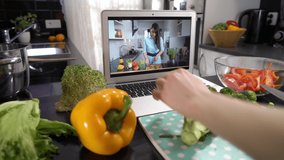 A young woman watching a online stream broadcast video blog tutorial about tasty and healthy food using laptop and cooking a meal at the home kitchen