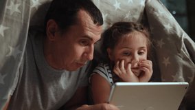 dad and daughter under the blanket with night a digital tablet. kid dream online video games at concept. dad and daughter watching online video under covers with digital tablet. social media