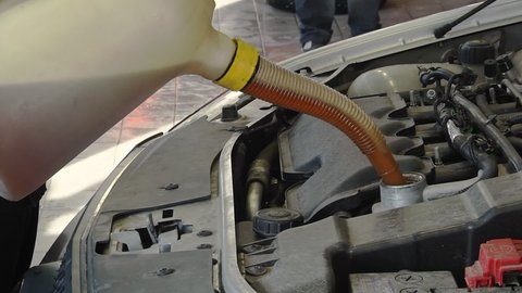 auto mechanic hands replacing and pouring motor oil into automobile engine at maintenance repair service station. Fresh oil is poured into the vehicle during oil changes.

