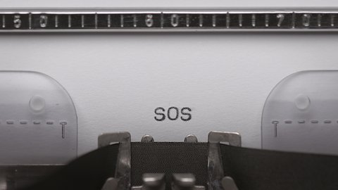Typing text SOS on vintage manual typewriter. Close up of writes word on white paper. Shot in macro 4K resolution. Typing a Morse code distress signal - The phrase save our souls.