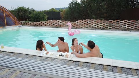 Happy couples eating sushi into a pool. Men feeding women with sushi in pool