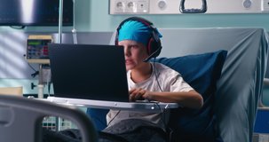 Concentrated boy with headset using laptop while playing videogame on laptop in ward of oncology clinic