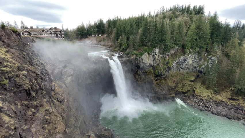 Wide shot of water plunging over the Snoqualmie Falls in Washington State, with mist rising around it and the lodge at the top. This is the falls and lodge seen in the opening of Twin Peaks