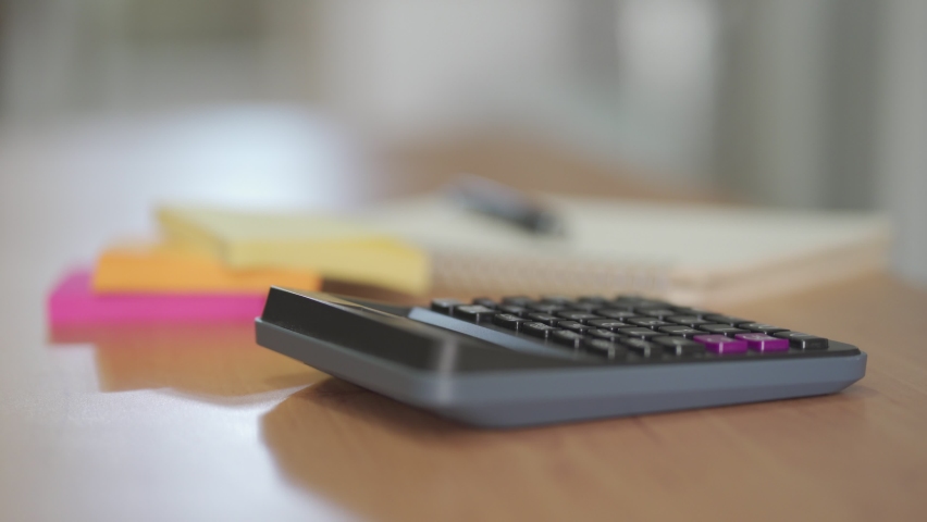 Men  hand typing on calculator button to calculate for personal tax or expense budget on the wooden table inside of the house with blurred paper note and pen. Financial and money saving concept. Royalty-Free Stock Footage #1068689309