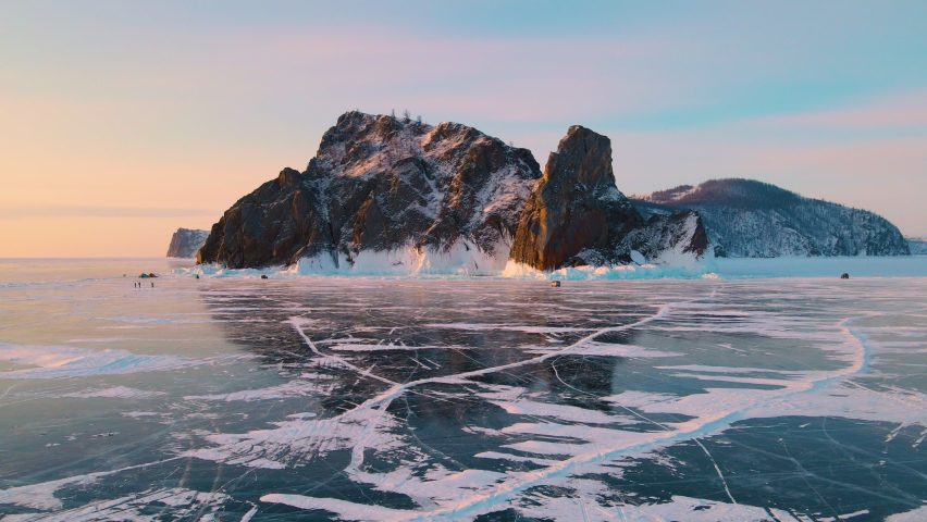 Baikal lake in winter with cracked blue ice. Flight above transparent ice of Cape Khoboy in Olkhon island. Baikal, Siberia, Russia. Beautiful winter landscape at sunrise. Aerial drone view. 4k