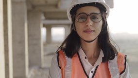 Track in a close-up shot of a young confident Indian Asian female civil engineer wearing a safety helmet standing with folded arms and looking at the camera on top of an under-construction building. - Powered by Shutterstock - Get 15% off with code: PIKWIZARD15
