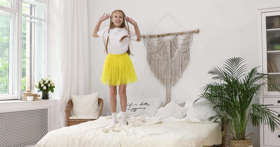 red girl teenager in a white jersey and yellow skirt jumps on a bed.