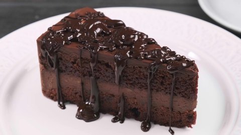 Pour chocolate over piece of chocolate cake. Chocolate cake on white plate.