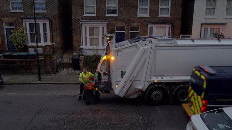 London. UK- 03.08.2021: a before day break collection of recycle domestic waste by the local authority with workers collecting the green top bins and emptying them in the garbage truck.