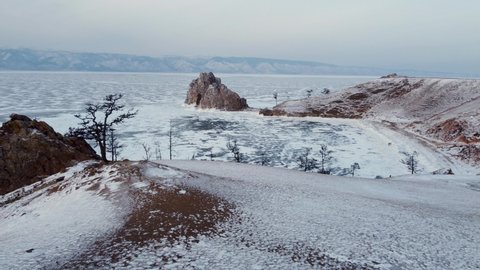 Baikal frozen lake, Olkhon island - Shaman rock, Burkhan cape aerial. Clear ice and snow. Travelling in winter at Russian Siberia. Aerial flight from lonely tree to sacred rock