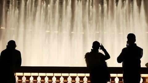 LAS VEGAS, NEVADA USA - 13 DEC 2019: People looking at Bellagio fountain musical performance at night. Contrast silhouettes and glowing dancing splashing water. Entertainment show in gambling city.