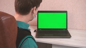 A man dances at a computer at a videoconference in a protective face mask, a chroma key on a laptop screen and a man's joy