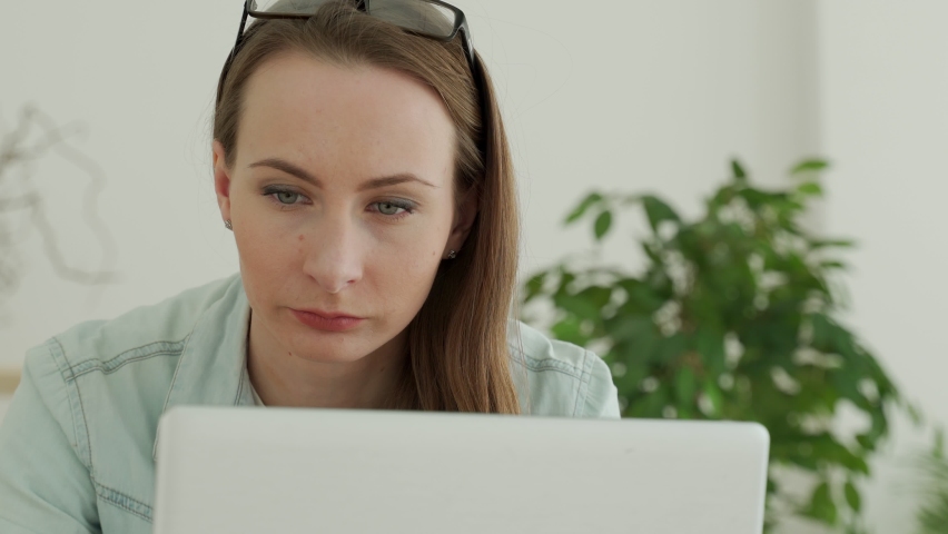 A beautiful young woman is working intently with a laptop. Woman's face close up Royalty-Free Stock Footage #1068707687