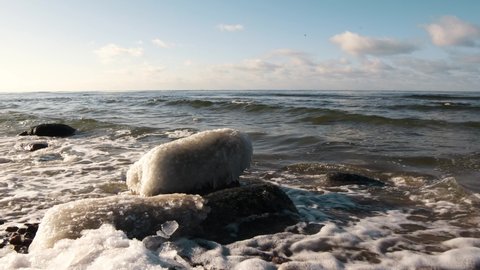 Baltic sea in winter. Frozen stones beside a shore. Stones covered with ice are washed by  sea waves. 