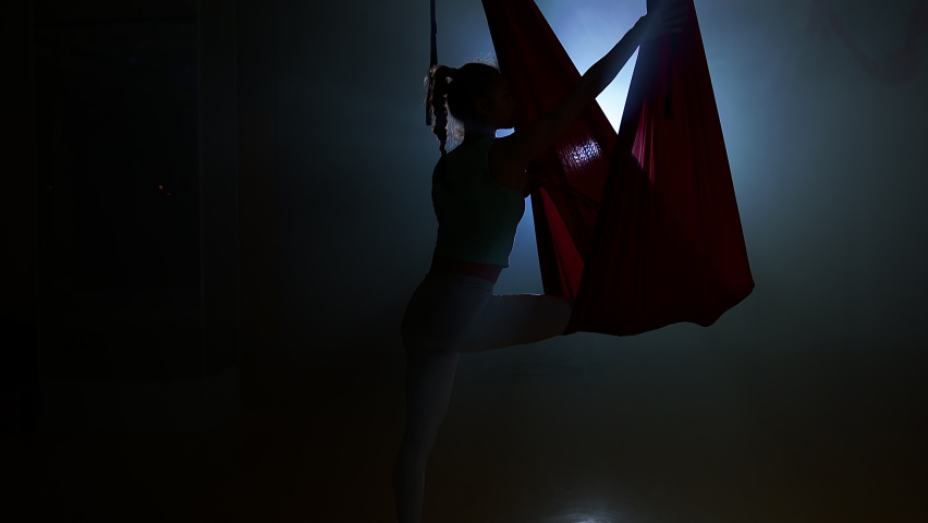 Beautiful, slender, muscular girl doing splits on Aerial Yoga Hammock in a dance studio with dim lights. Detoxify your body. High quality.