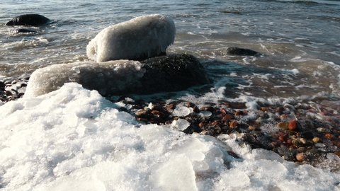 Baltic sea in winter. Frozen stones beside a shore. Stones covered with ice are washed by sea waves. 