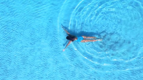 Young woman dressed in blue swimsuit dives in to the crystal oceans water. Aerial shot of beautiful sea view and woman swims under water.