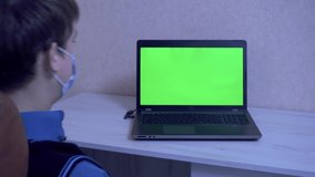 A guy in a protective face mask is emotionally angry over a remote connection at a video conference and bangs his fists on a laptop, green screen
