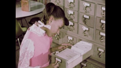 1960s: Library. Little girl uses card catalog. Girl finds book on shelf and begins to read. Children look at books in section marked "FICTION."