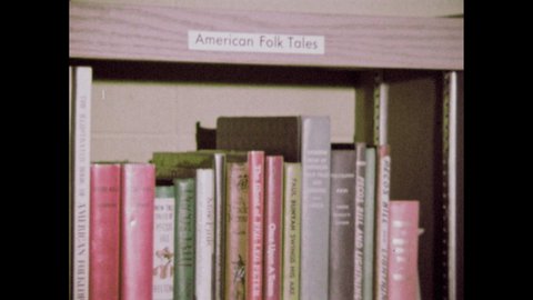 1960s: Library. Books on shelves. Label reads "AMERICAN FOLK TALES." Drawing of Paul Bunyan and ox. Label reads "BIOGRAPHIES." Woman touches spines of books. Man.