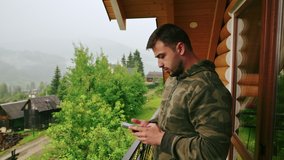 Adult man spends a rainy day of vacation on the balcony of a country apartment, uses a smartphone and makes videos on a smartphone camera.