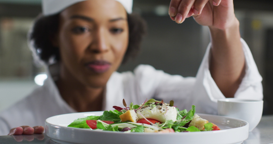 African american female chef garnishing dish and similing in restaurant kitchen. Working in a busy restaurant kitchen. Royalty-Free Stock Footage #1068727694