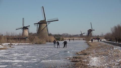 KINDERDIJK, NETHERLANDS – 13 FEBRUARY 2021: Classic Dutch Winter landscape, with people having fun and ice skating in typical Dutch landscape of windmills. 
