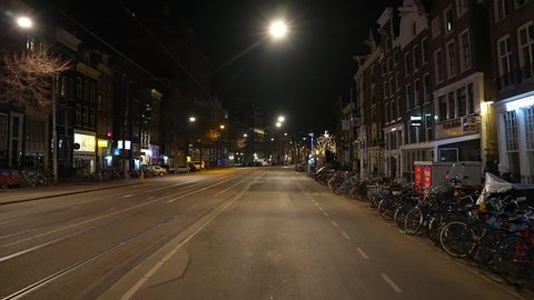 AMSTERDAM, NETHERLANDS – 5 MARCH 2021: Point of view shot cycling through deserted street in downtown Amsterdam city, during evening curfew in the Netherlands (Covid-19 coronavirus).